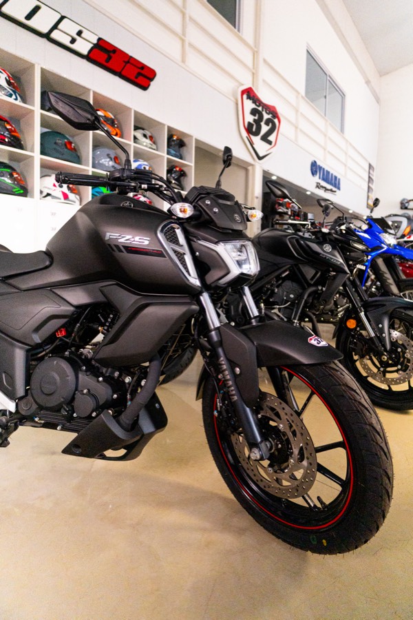 Yamaha FZ-S negra en el salón de Motos 32, con cascos y el escudo de la marca de fondo